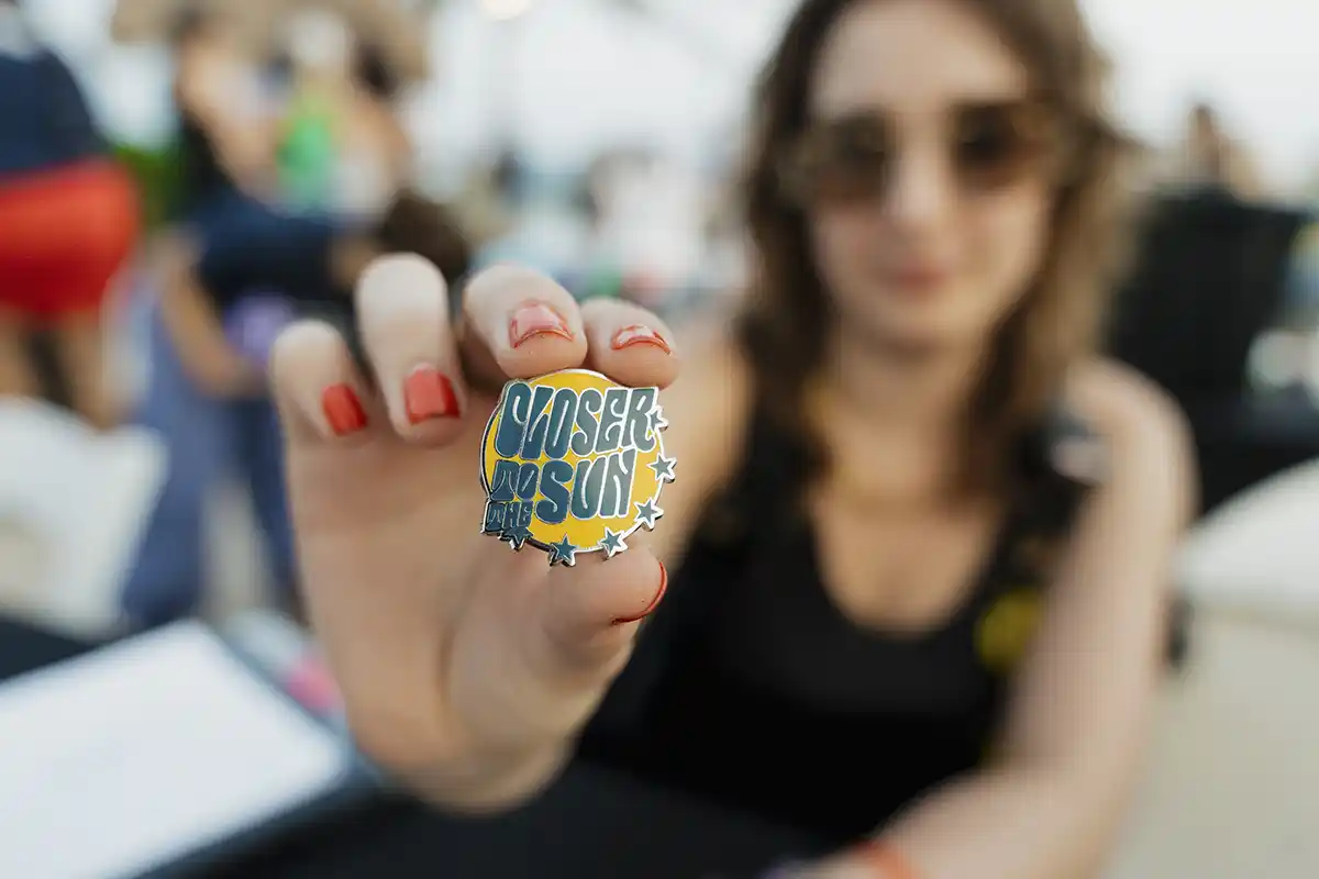 A close up photo of a Closer to the Sun pin.