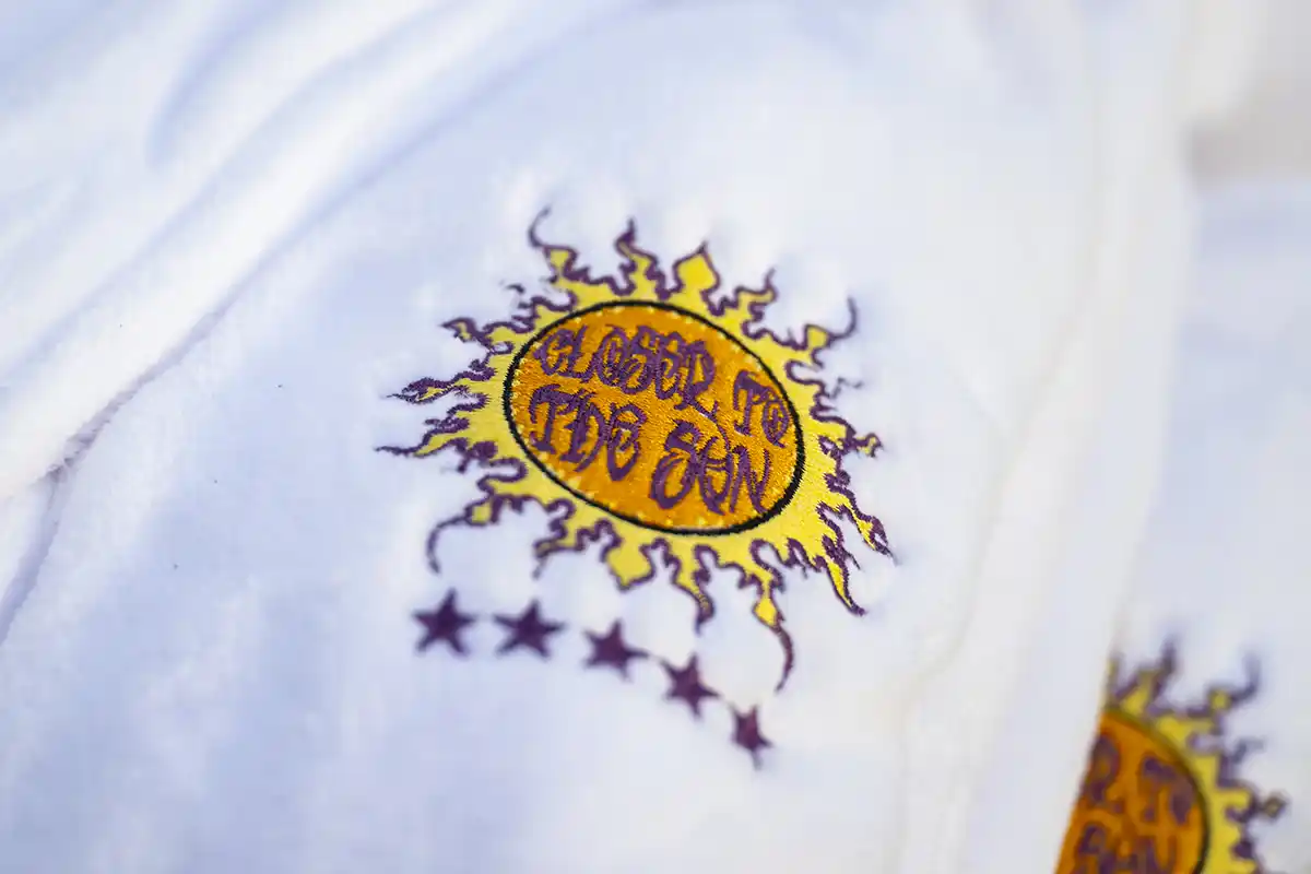 A closeup of the Closer to the Sun logo on a white robe.