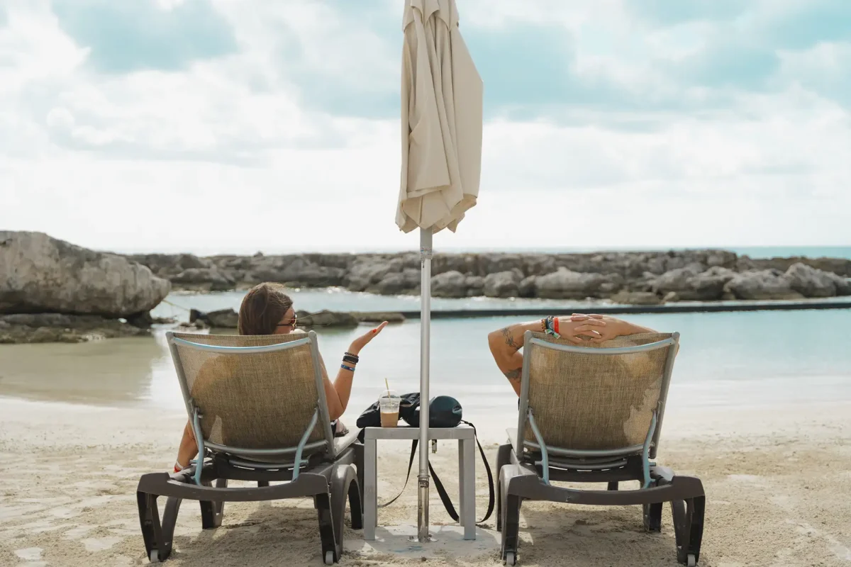 A photo from behind two lounge chairs with guests relaxing by the beach.