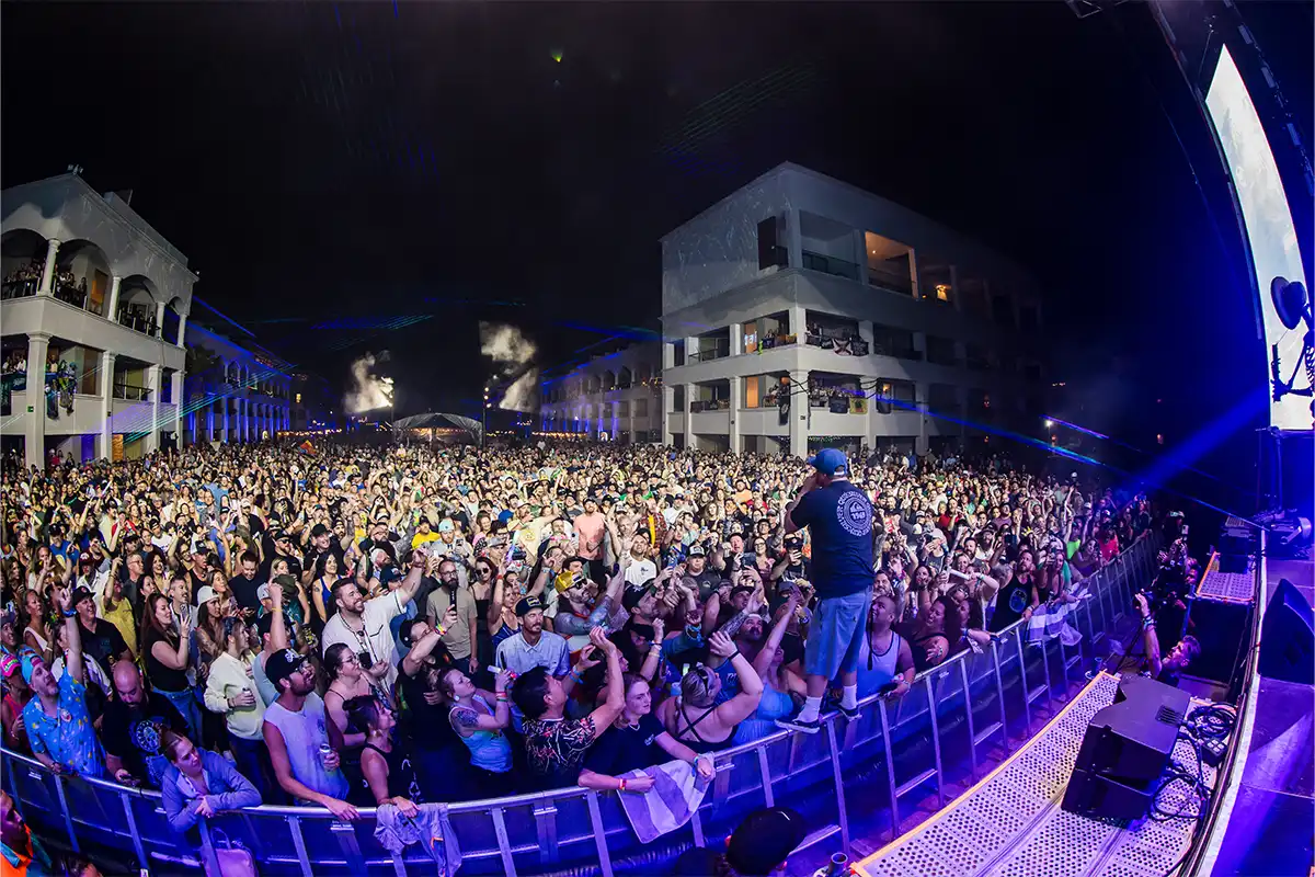 Kyle from Slightly Stoopid standing on the crowd barrier, looking out across the crowd of people in the courtyard.