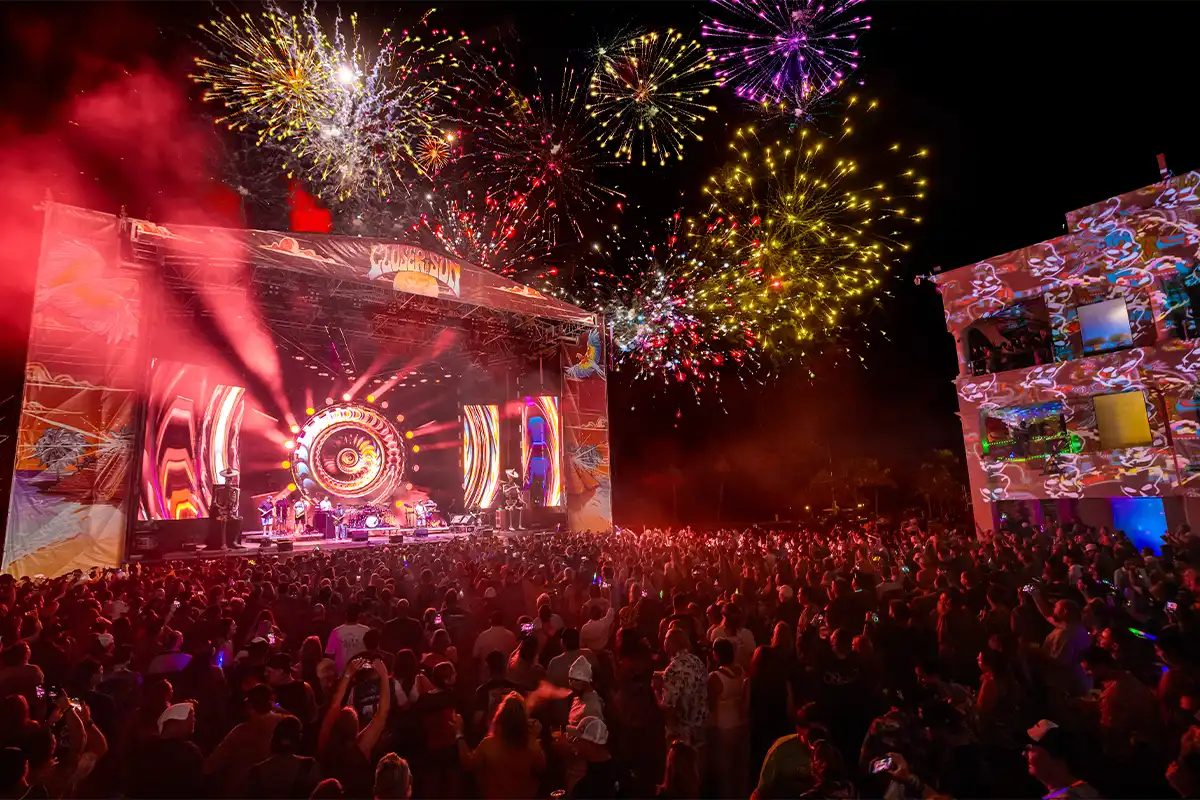 Concert Courtyard main stage with large crowd. Stage lights and fireworks light up the sky.