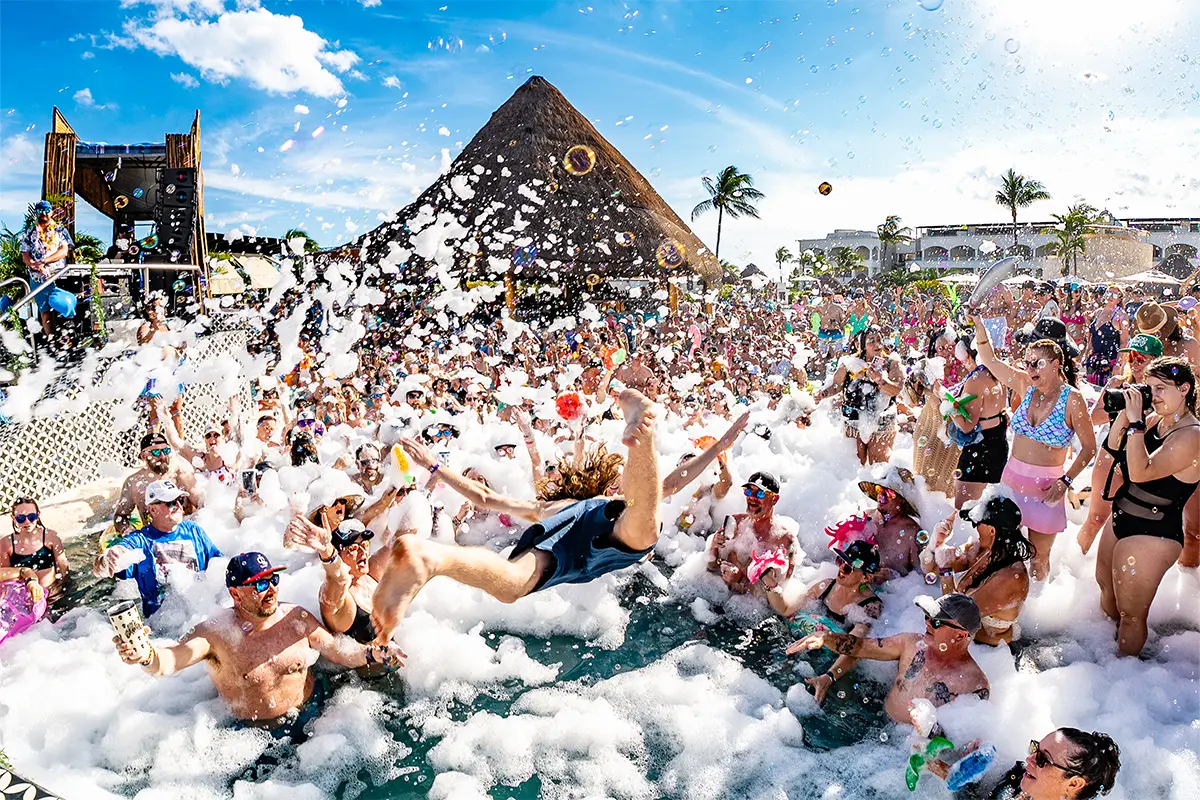 A guest jumping into a pool during a foam party. Foam fills the surrounding areas of the pool.