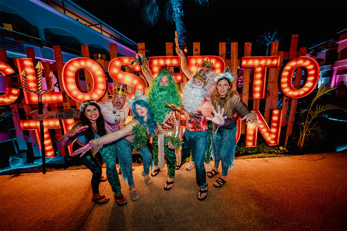 Group photo of guests in front of a "Closer To The Sun" light up sign wall in theme night costumes.