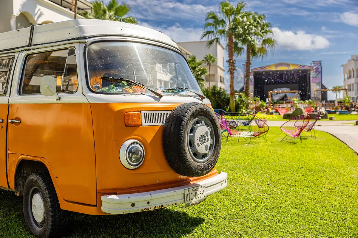 An Orange VW bus parked in the concert courtyard with the Main Stage in the background.